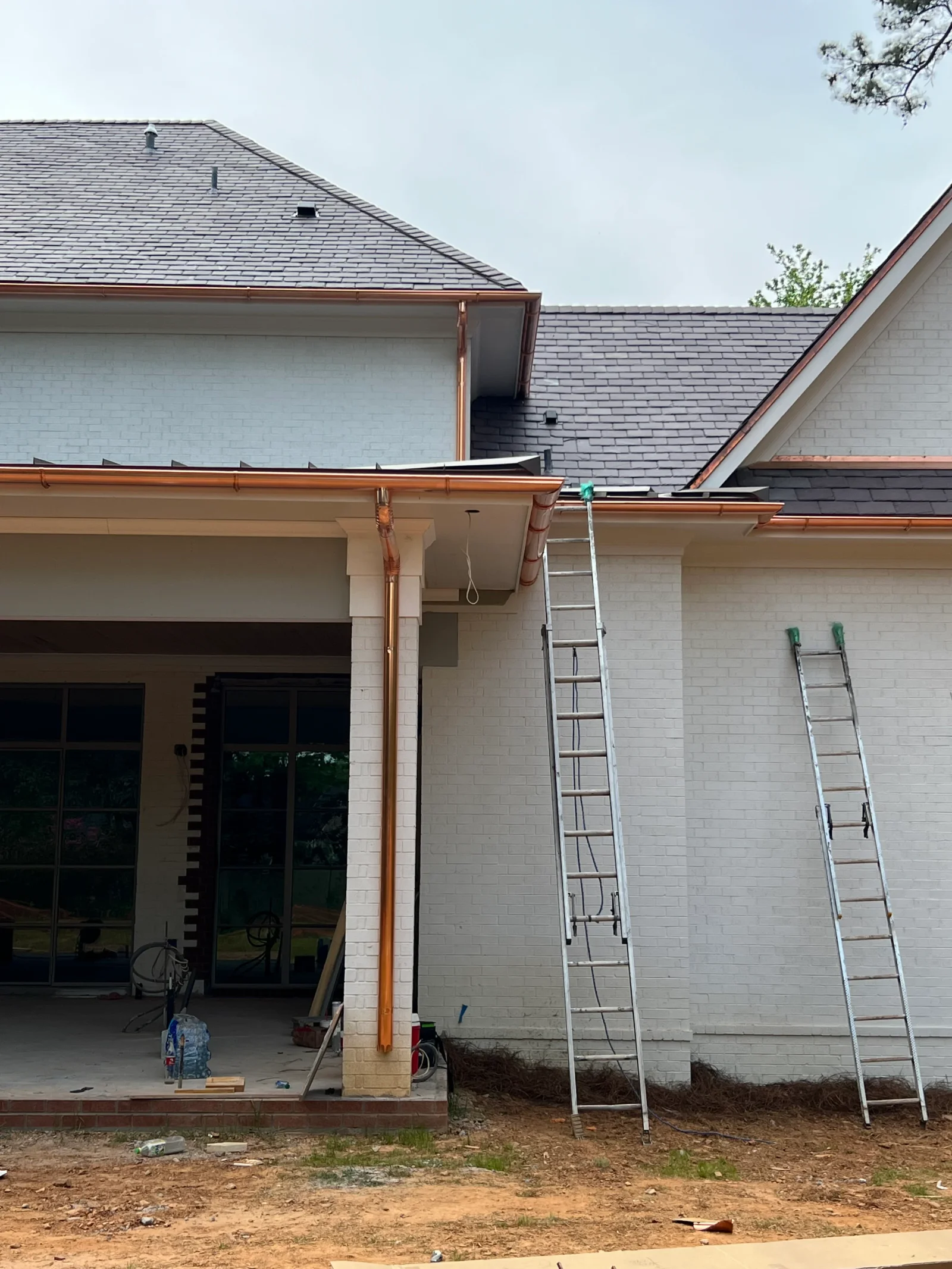 Copper gutters and downspouts installed on white brick home with slate roof