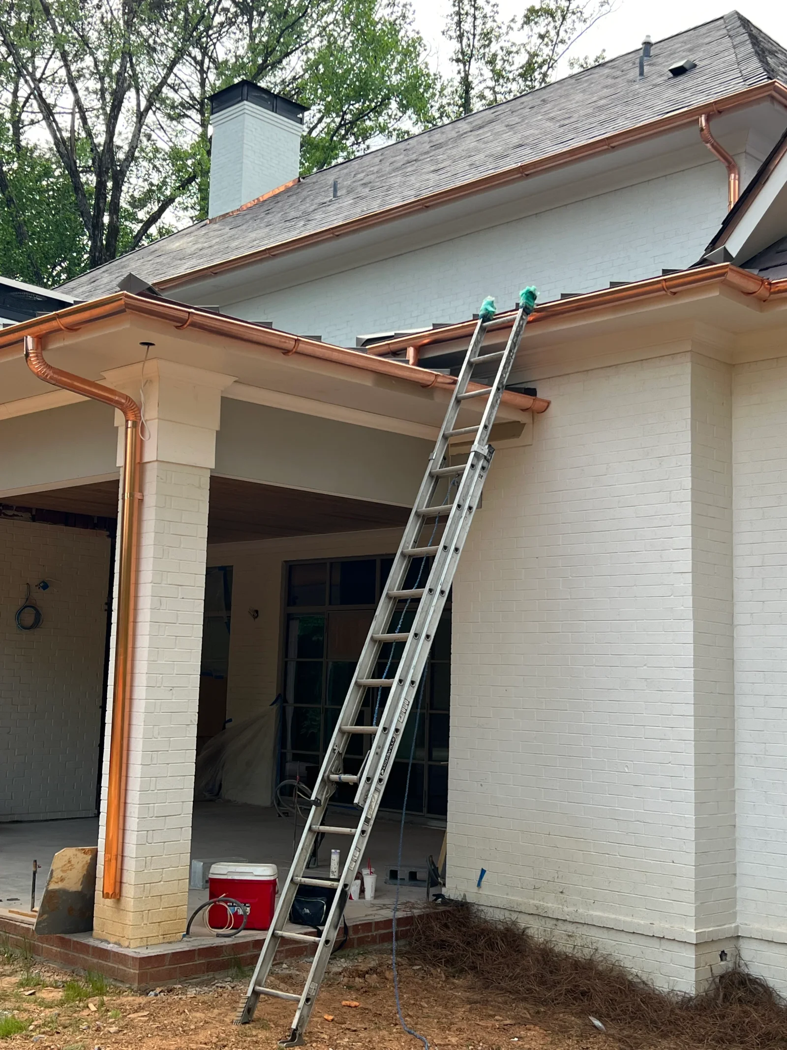 Copper gutters and downspouts installed on white brick home addition with new fascia
