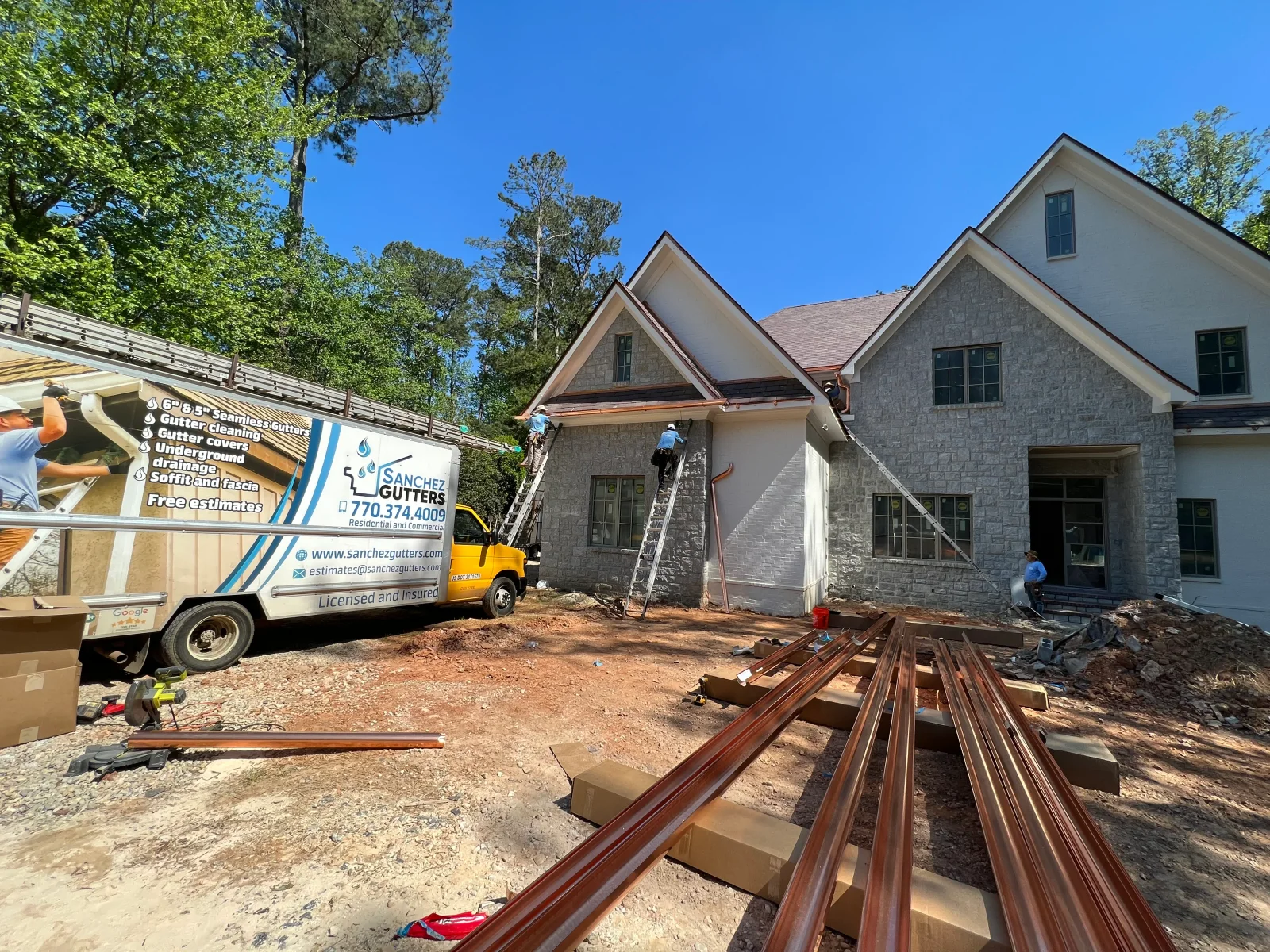 Seamless gutter installation on new stone and siding home with equipment and materials on site
