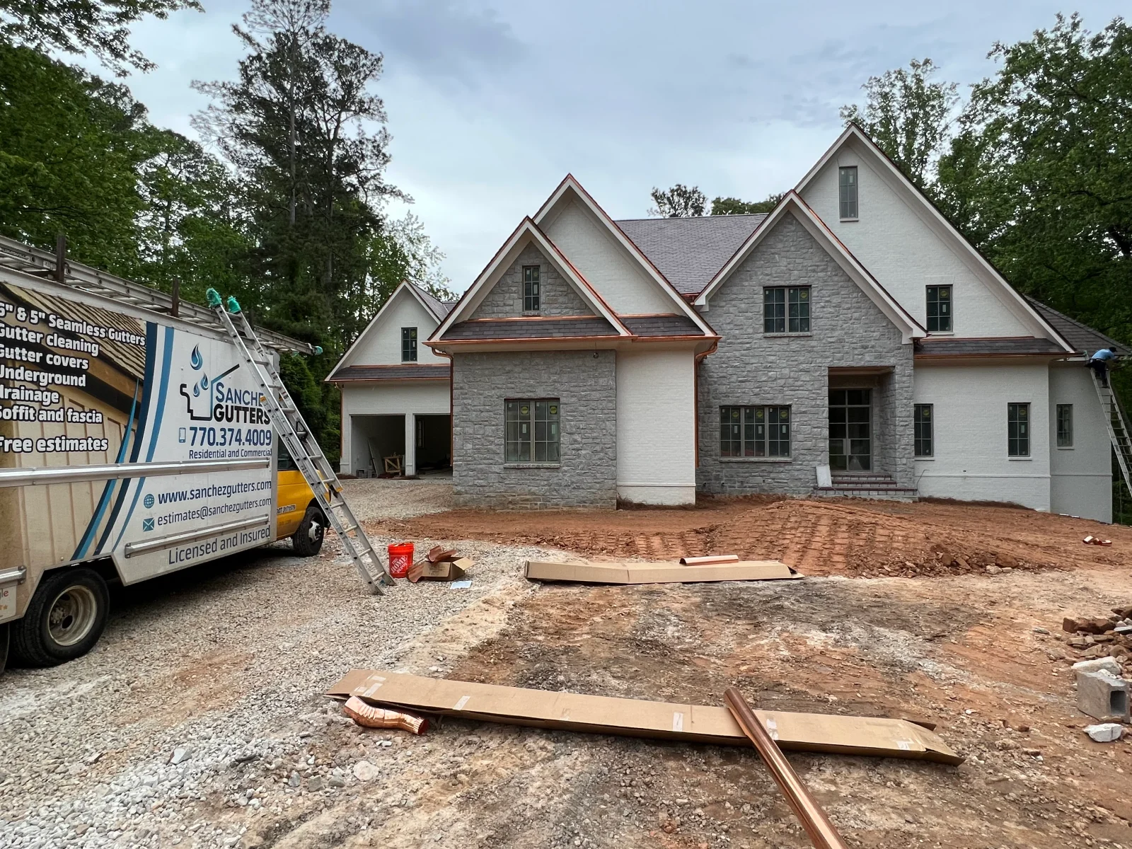 New home with stone and white exterior receiving seamless gutter and copper downspout installation