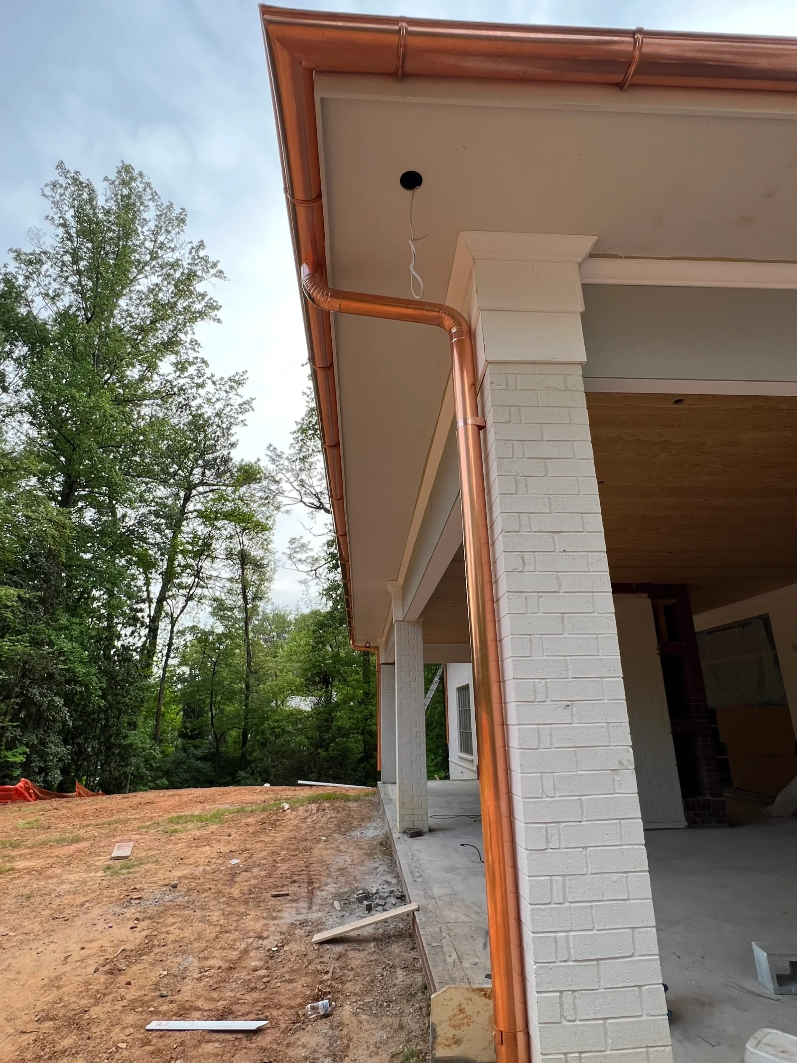 Copper gutter and downspout system on white brick residential exterior with soffit